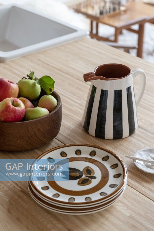 Bol de fruits, assiettes et pichet en céramique rayé sur table en bois