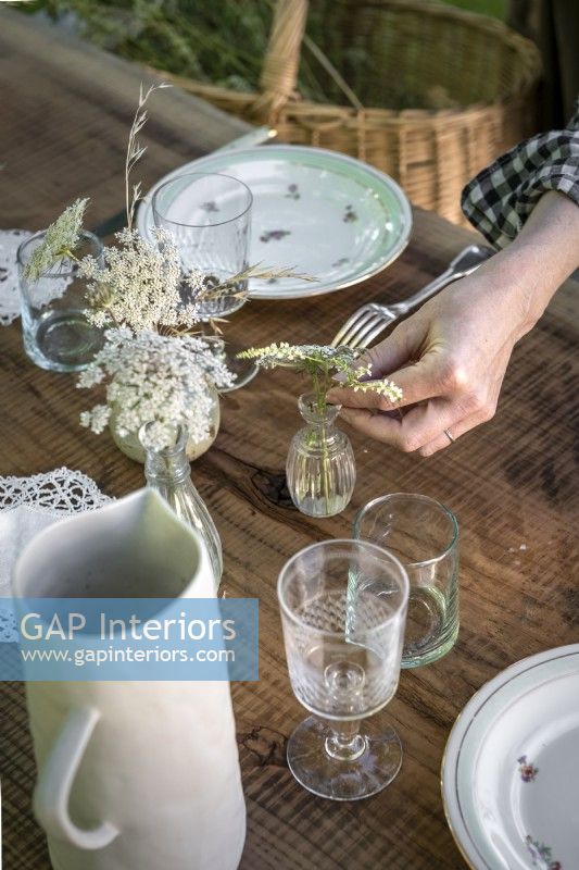 Femme mettant des fleurs sauvages dans un vase en verre sur une table à manger extérieure