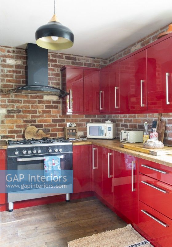 Mur de briques apparentes et armoires rouges dans une cuisine moderne
