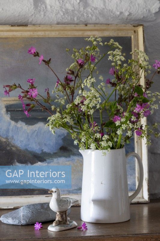Vase de fleurs sauvages sur une commode, vieille peinture maritime derrière et murs blanchis à la chaux
