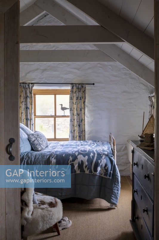 Vue sur une chambre confortable, un lit avec des couvertures bleues, une vieille commode et des murs et poutres blanchis à la chaux.