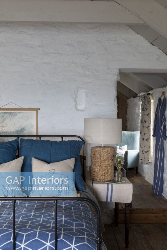 Lit à structure métallique, avec couverture et oreillers bleus, murs blanchis à la chaux et lampe rustique à côté du lit.