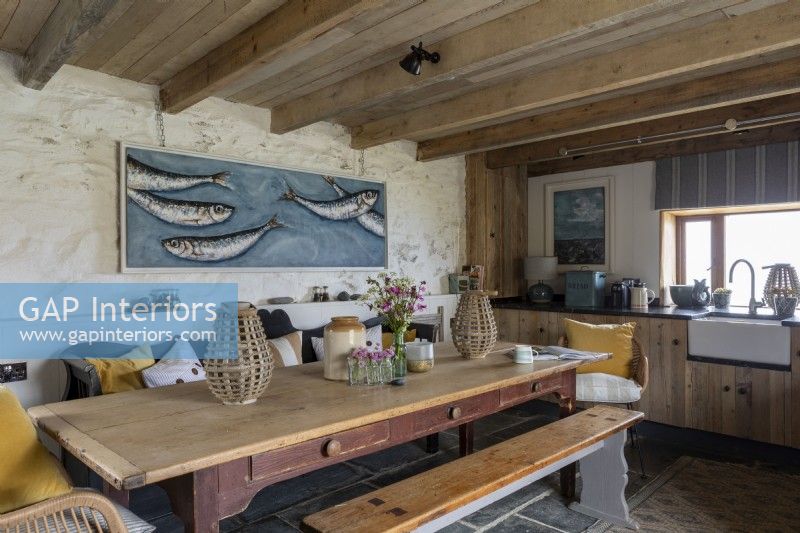 Cuisine rustique grande et confortable avec table de ferme en bois et grandes œuvres d'art modernes représentant des poissons dans une mer bleue.