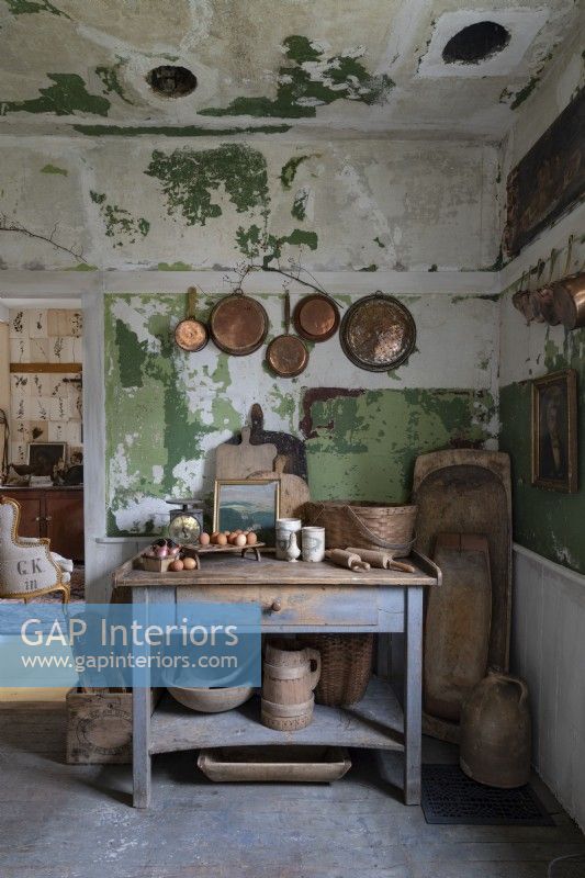 Casseroles et poêles en cuivre dans une cuisine rustique avec des meubles et des murs en détresse