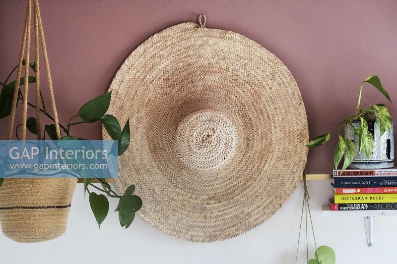 Détail d'un grand chapeau de paille sur un mur avec des plantes d'intérieur sur une étagère