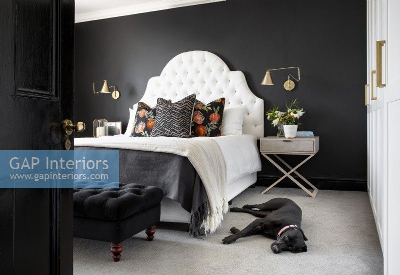 Dramatic bedroom with black walls and  white deep buttoned headboard