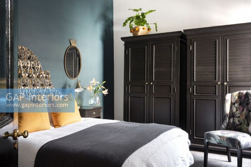 Chambre avec tête de lit rembourrée, mur bleu canard et placards noirs 