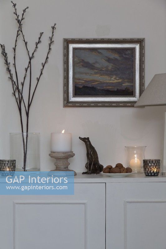 Display of candles and dog sculpture and artwork on grey sideboard