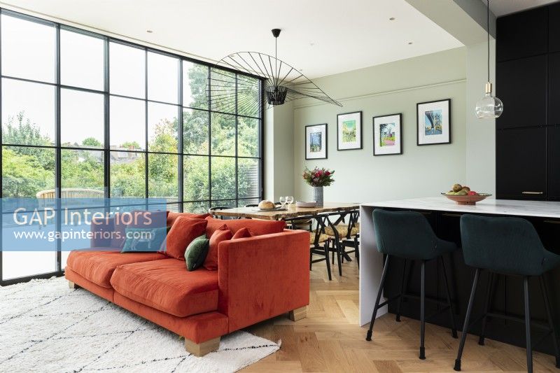Salon salle à manger ouvert et contemporain avec canapé orange et fenêtres hautes. 