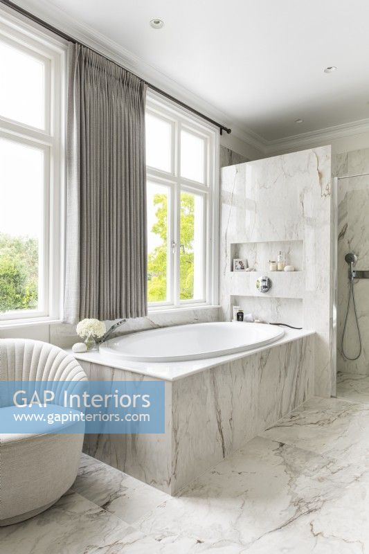 Salle de bain en marbre classique et contemporaine avec baignoire près de la fenêtre et douche. 