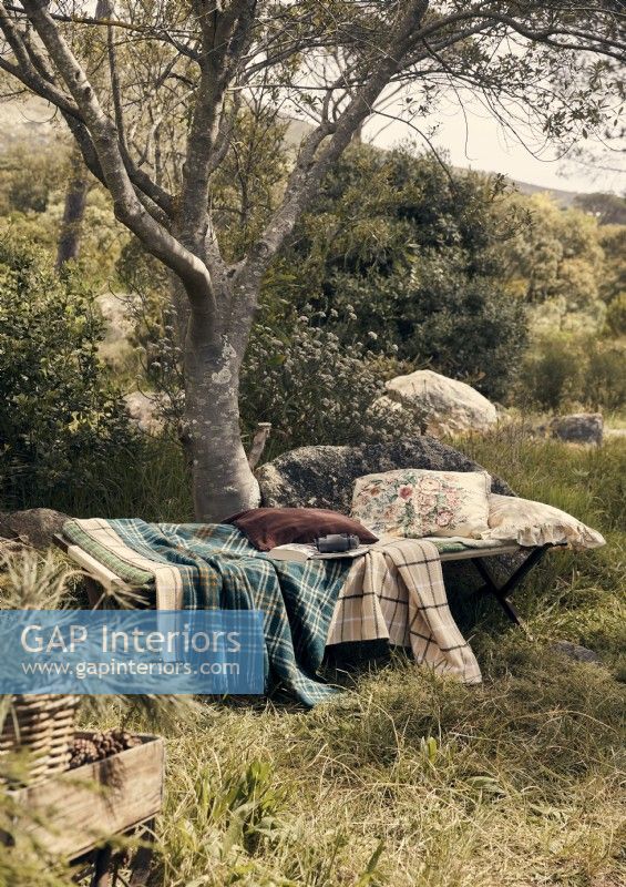 Lit de camp vintage avec coussins et couvertures dans un jardin boisé 