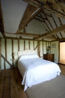 Ferme Boonshill, East Sussex. Intérieur de la chambre avec parquet, poutres apparentes et lit avec tête de lit français en bois.
