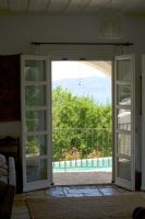 Corfou, Grèce. Yialiskari House Villa près de Kalami. Vue à travers le salon sur la piscine et les montagnes albanaises