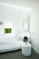 Chambre blanche moderne avec miroir au-dessus du lit et table de chevet avec vase de stocks