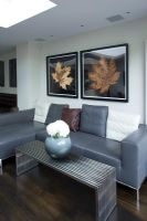 Salon contemporain avec canapé en cuir gris, table basse en métal avec vase moderne et imprimés de feuilles sur le mur