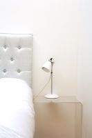 Détail du lit avec tête de lit rembourrée et table de chevet en plexiglas avec lampe