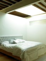 Chambre blanche moderne avec tête de lit rembourrée, ameublement et puits de lumière au-dessus du lit