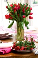 Tulipes rouges dans un vase et assiette de fraises sur table à manger