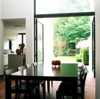 Vue de la table à manger avec cuisine et portes ouvertes sur jardin en arrière-plan