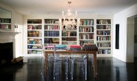 Table en bois entourée de chaises Louis Ghost dans la chambre avec grande bibliothèque