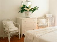 Vue de la chambre avec des coussins sur une chaise et des fleurs dans un seau sur une table d'appoint