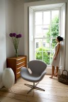 Femme regardant par la fenêtre. Chaise 'Swan' Arne Jacobsen au premier plan.