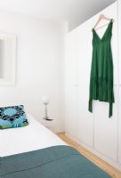 Chambre avec coussin à motifs turquoise et robe verte suspendue à l'armoire