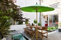 Petit jardin urbain avec mobilier en bois et parasol vert
