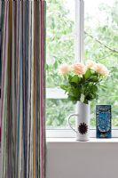 Roses en pot vintage sur le rebord de la fenêtre à côté de rideaux rayés