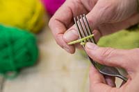 Faire des décorations de pompons de Noël à partir de laine - Maintenez une extrémité de la laine en place avec un doigt et commencez à enrouler la laine autour de la fourchette