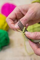 Faire des décorations de pompons de Noël à partir de laine - Maintenez une extrémité de la laine en place avec un doigt et commencez à enrouler la laine autour de la fourchette