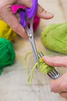 Faire des décorations de pompon de Noël - Utilisez les ciseaux pour couper la laine, laissant un paquet de laine enroulé sur la fourche
