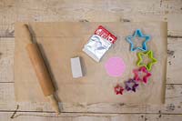 Fabrication d'étoiles en argile - Les matériaux requis sont de la pâte à modeler blanche, un moule à fleurs en silicone, des coupeurs en forme d'étoile, une ficelle, des ciseaux, un rouleau à pâtisserie et une brochette