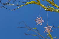 Faire des étoiles de fil de cuivre - décorations finies suspendues à une branche recouverte de lichen sur un fond bleu