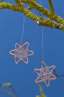 Faire des étoiles de fil de cuivre - décorations finies suspendues à une branche recouverte de lichen sur un fond bleu