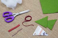 Fabrication de décorations de Noël en feutre cousu - Les matériaux requis sont des ciseaux, du feutre, une aiguille et du fil, de la laine, un modèle de triangle et une ficelle décorative