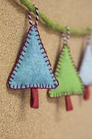 Fabrication de décorations de Noël en feutre cousu - arbres de Noël miniatures en feutre et chaîne décorative, accrochés contre une planche de liège