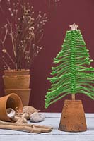 Arbre de Noël en laine verte monté dans un pot en terre cuite retourné, sur un fond bordeaux