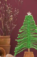 Arbre de Noël en laine verte monté dans un pot en terre cuite retourné, sur un fond bordeaux