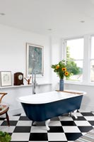 Baignoire autoportante bleue dans la salle de bain avec plancher noir et blanc