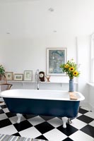 Baignoire autoportante bleue dans la salle de bain avec plancher noir et blanc