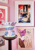 Photographies et peintures encadrées sur un mur rose avec des poteries colorées