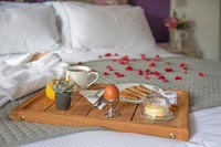 Plateau de petit déjeuner et peignoir avec des pétales de rose sur le lit