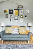 Canapé gris avec coussins jaunes et affichage d'images sur mur peint gris