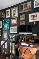 Mur peint en noir recouvert d'images encadrées sur un bureau en bois