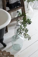 Branches de feuillage dans des vases en verre sur le plancher de la salle de bain