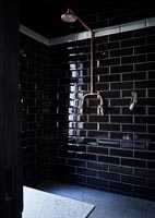 Douche avec carrelage style brique noire et pomme de douche en cuivre