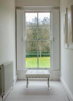 Repose-pieds en cuir blanc et chrome à côté de la fenêtre avec volets