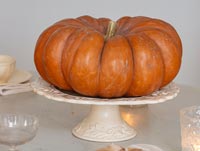 Citrouille orange décorative sur un support à gâteau en céramique blanc vintage