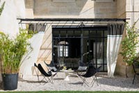 Chaises de jardin et table sur terrasse en gravier avec rideaux pour l'ombre